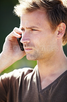 Buy stock photo A handsome young man talking on his cellphone with a serious expression