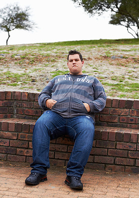 Buy stock photo An obese man sitting outside with his hands in his pockets on a winter's day