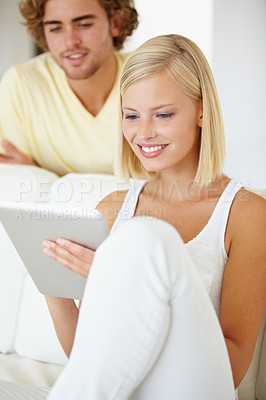 Buy stock photo A beautiful young woman using a tablet as her boyfriend watches from over her shoulder