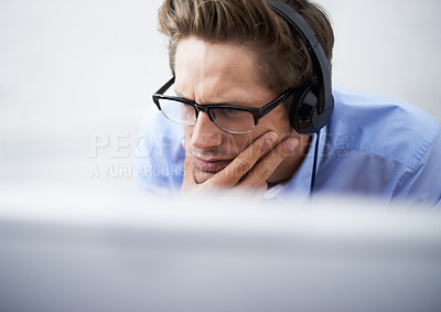 Buy stock photo A handsome young businessman wearing a headset while concentrating on his computer screen