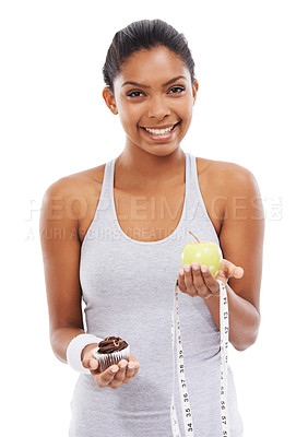 Buy stock photo Portrait, woman and choice of apple or cupcake in studio isolated on a white background to lose weight. Smile, fitness or exercise with a happy young athlete holding fruit, dessert and measuring tape