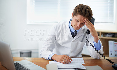 Buy stock photo Shot of a concerned doctor sitting in his office and talking on the phone while looking over paperwork