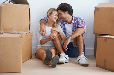 Buy stock photo A happy young couple sitting on the floor in their new home and cuddling while surrounded by boxes