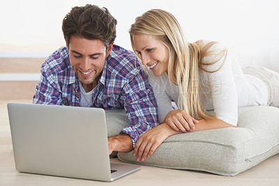 Buy stock photo A happy young couple lying on the floor at home and using a laptop together