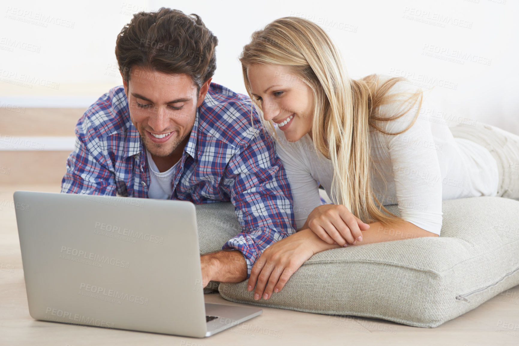 Buy stock photo A happy young couple lying on the floor at home and using a laptop together