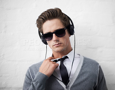 Buy stock photo A trendy young man loosening his tie while listening to music on his headphones
