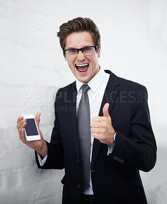 Buy stock photo Excited businessman, portrait and phone with thumbs up for success against a gray wall background. Happy man or employee smile with mobile smartphone, like emoji or yes sign for winning or good job