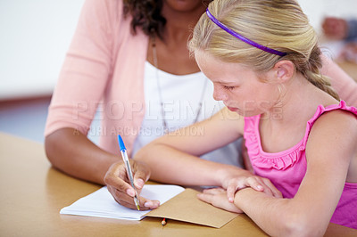 Buy stock photo Child, girl and student with teacher and writing in classroom, learning and helping for assessment or exam. Study, knowledge and education, people with notebook and pen for notes and info in class