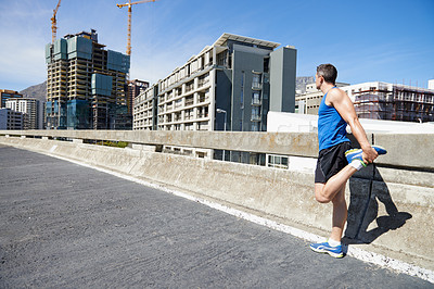 Buy stock photo Young man stretching his legs before a road run in the city