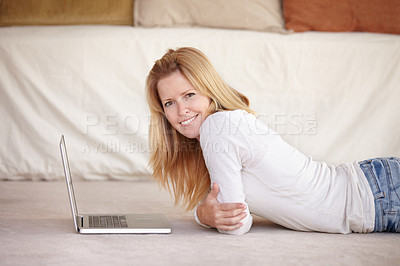 Buy stock photo A beautiful mature woman working on her laptop while lying on the floor