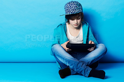 Buy stock photo A young boy sitting on his digital tablet in the studio