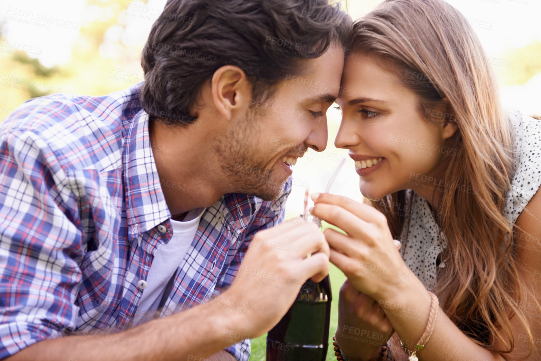 Buy stock photo Nature, happy and couple sharing a drink with love on a summer picnic date in an outdoor garden. Happiness, smile and young man and woman drinking a bottle of cola together relaxing on grass in field