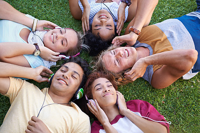 Buy stock photo High angle of a group of friends lying on their backs on the grass in a park and listening to music