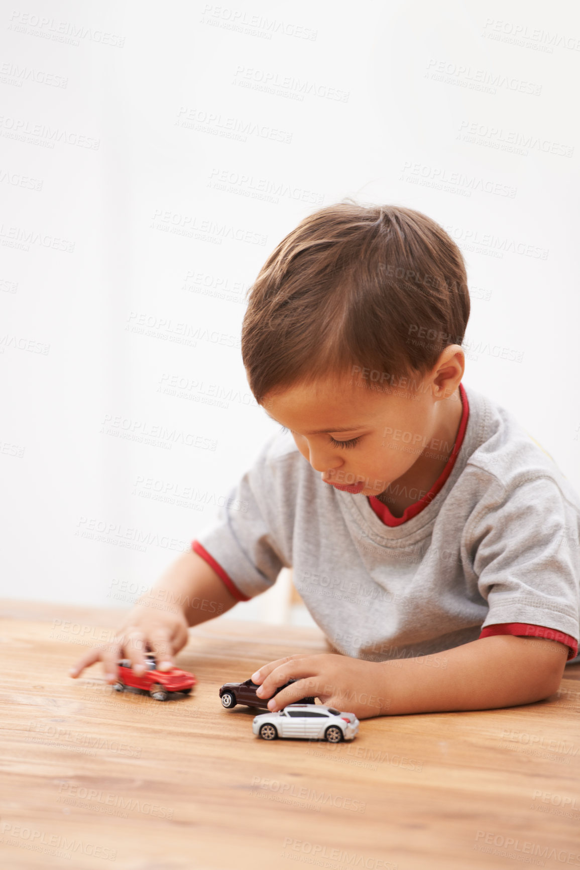 Buy stock photo Cars, toys and boy child by table playing for learning, development and fun at modern home. Cute, sweet and young kid enjoying a game with plastic vehicles by wood for childhood hobby at house.