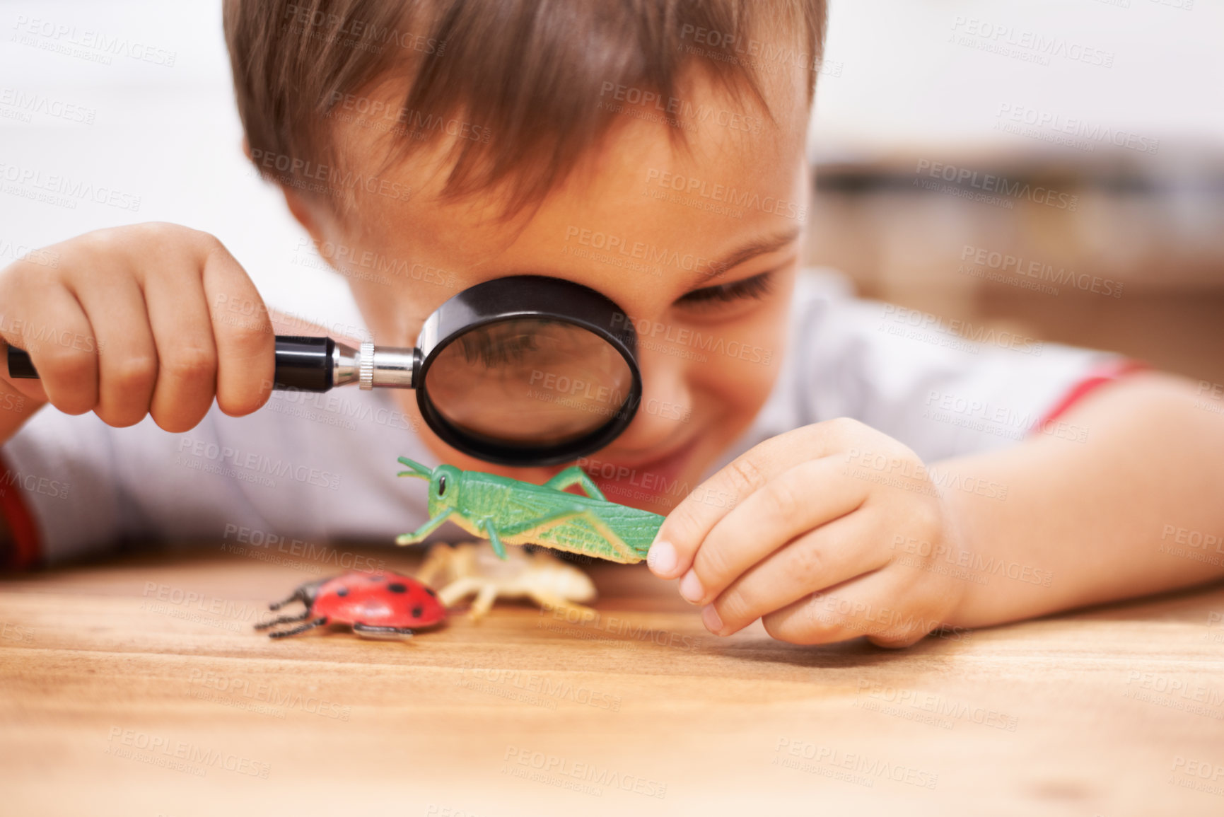Buy stock photo Shot of a young boy inspecting his toys with a magnifying glass