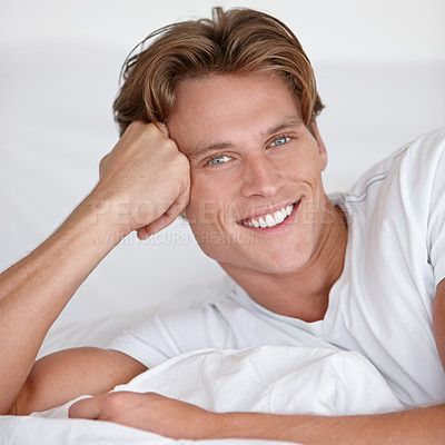 Buy stock photo A handsome young man smiling while relaxing in bed