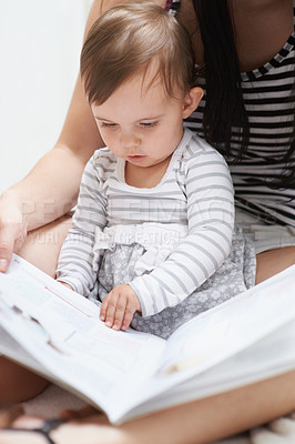 Buy stock photo Shot of a cute little baby girl sitting sitting on her mom's lap looking through a picture book