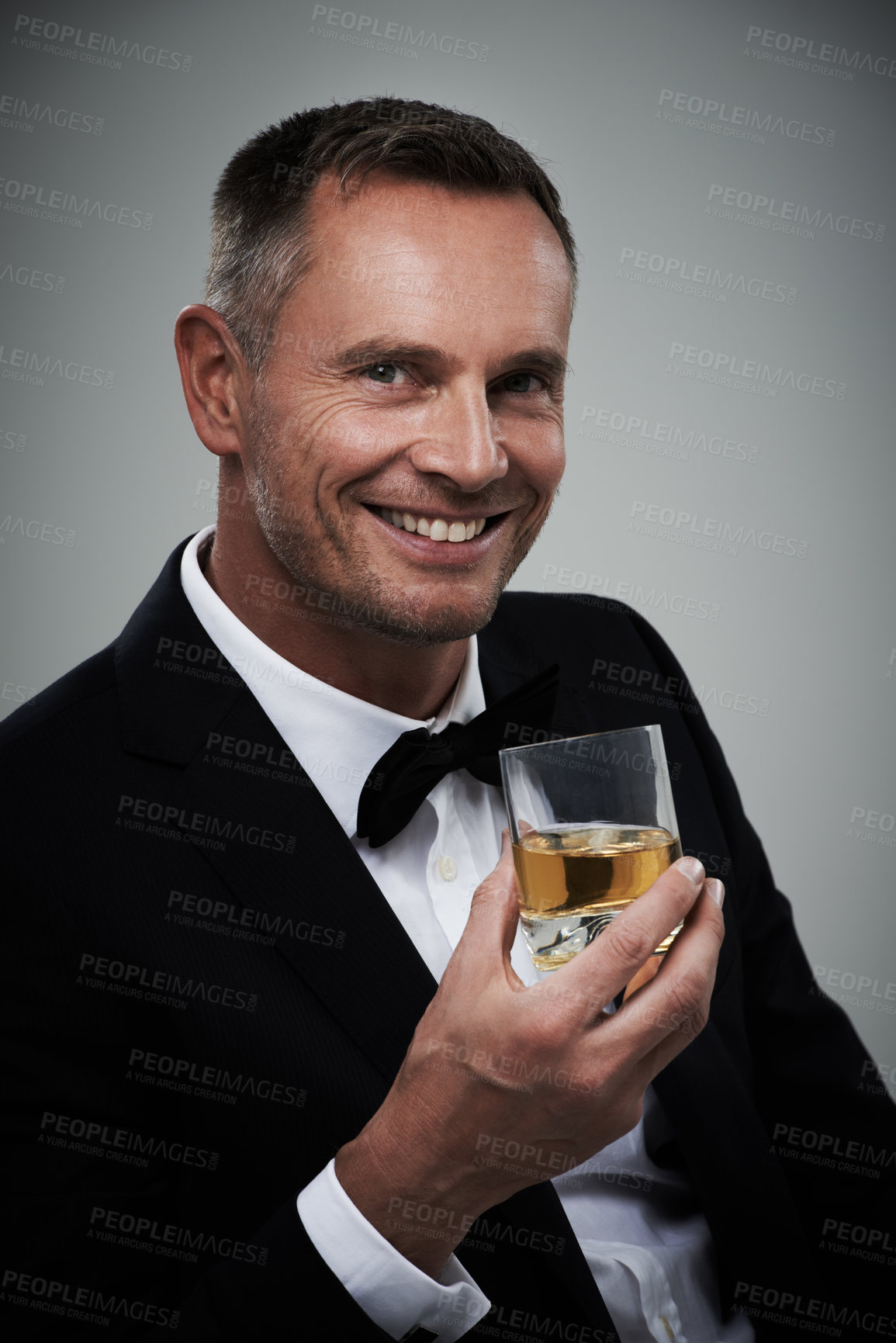Buy stock photo Tuxedo, whiskey glass and man portrait with alcohol in a suit feeling classy with a luxury drink. Gray background, isolated and studio with a model, agent or actor smile with rich drinking