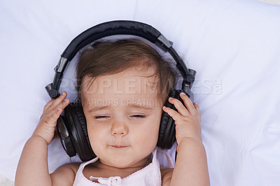 Buy stock photo A cute young baby girl listening to music on headphones