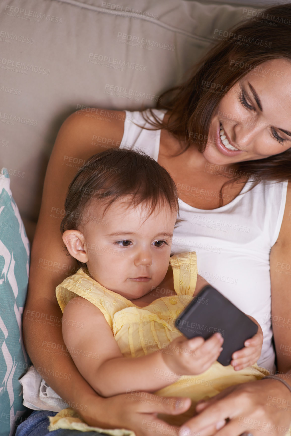 Buy stock photo A baby girl lying on her mother's lap playing with a cellphone
