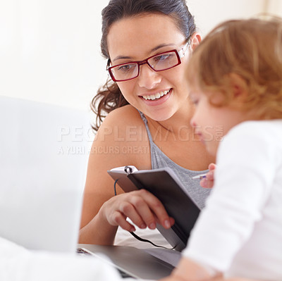 Buy stock photo A young mother writing in her diary with her baby daughter sitting next to her