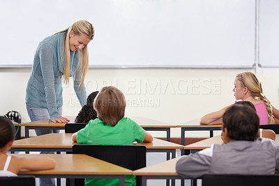 Buy stock photo Teacher, children and classroom for education, learning and writing or language development with support at desk. Happy woman with kids for teaching, helping with knowledge and questions at school