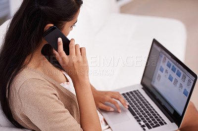 Buy stock photo A young woman speaking on her phone while working on her laptop at home