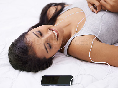Buy stock photo Woman, relax on bed and listening to music on phone with smile for podcast, sound and streaming service at home. Young person with mobile app for audio, happy song and dream or sleeping in bedroom