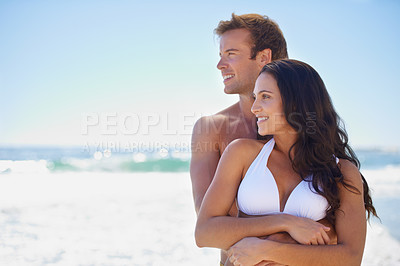 Buy stock photo A happy couple holding each other on the beach looking out over the ocean