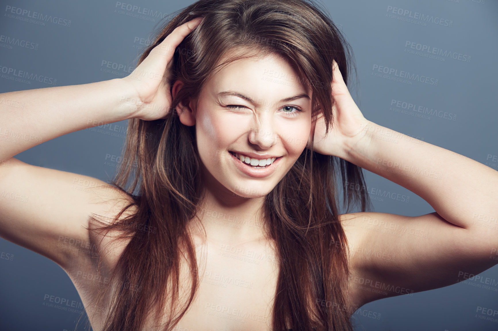 Buy stock photo Wink, face and beauty portrait of a woman in studio with a smile, makeup and hands in hair. Headshot of a happy female model on a grey background for natural glow, skin cosmetics and playful flirting