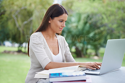 Buy stock photo A young woman sitting in a park working on her laptop with a cup of coffee next to her