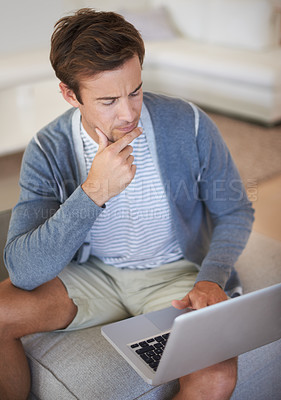 Buy stock photo A young man looking thoughtful while using a laptop at home