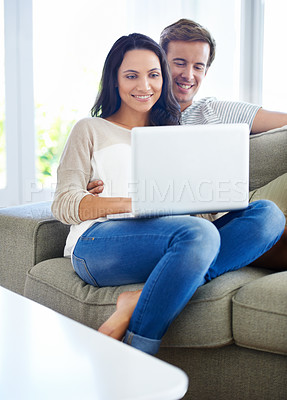 Buy stock photo A young couple using their laptop while sitting on the sofa at home
