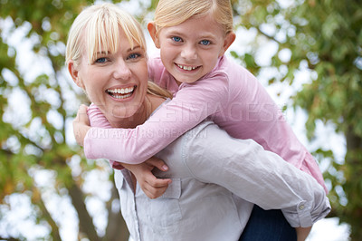 Buy stock photo A happy young mother giving her daughter a piggyback ride in the park