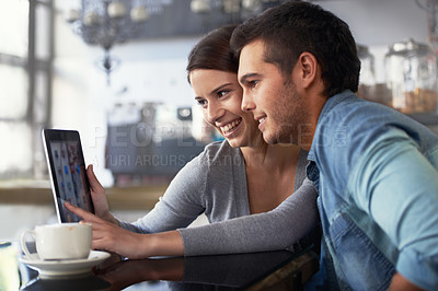 Buy stock photo Shot of a young couple looking at a digital tablet while sitting in a cafe