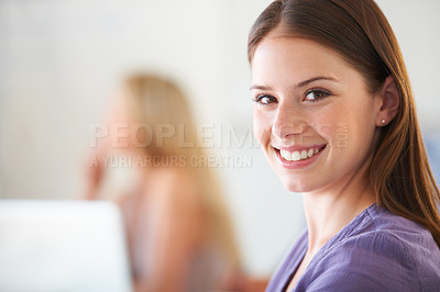 Buy stock photo A casual young businesswoman smiling with a blurred colleague in the background