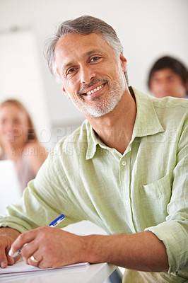 Buy stock photo Smiling mature businessman taking some notes while looking at the camera