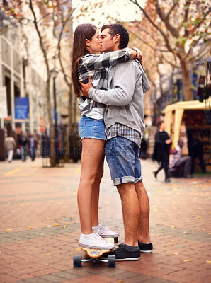 Buy stock photo Couple, skateboarding and kissing in city, in love and excited to learn together and romantic relationship. Cape town, fun and hobby with boyfriend and girlfriend in street, helping and dating