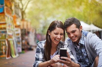 Buy stock photo A happy young couple sitting outside looking at pictures on their cellphone