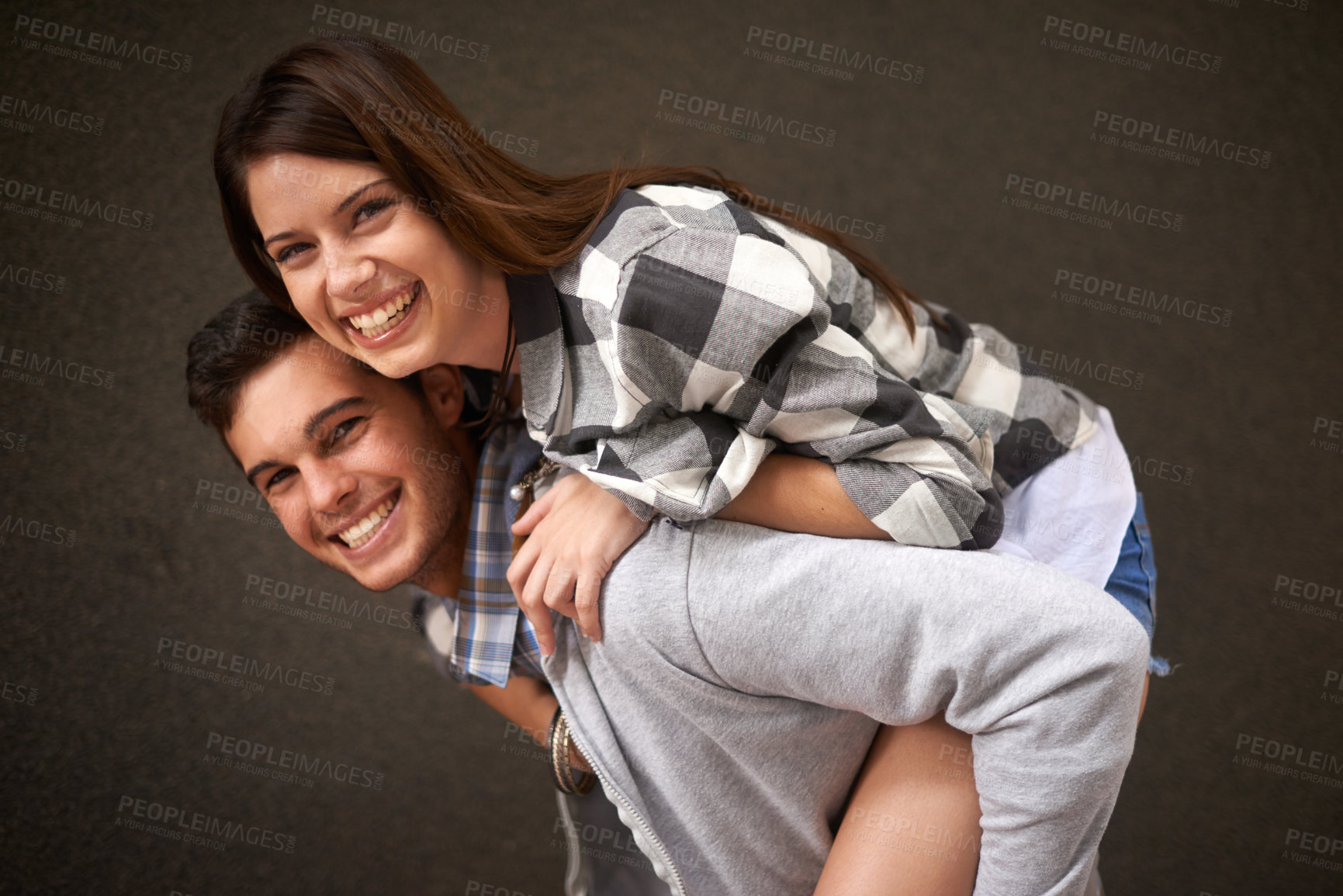 Buy stock photo Smile, hug and portrait of couple piggyback ride, bond and having playful fun isolated on grey background. Support, embrace and young silly man, woman or people happy for funny game with partner