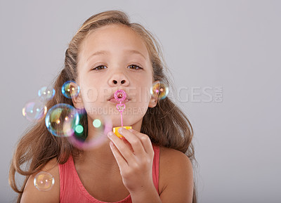 Buy stock photo Portrait, little child and blowing bubbles in studio by toy, cute and fun games with soap liquid. Girl, face and learning to play with bubble wand, childhood development and sweet by gray background