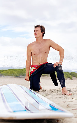 Buy stock photo A young surfer doing stretches on the beach next to his board