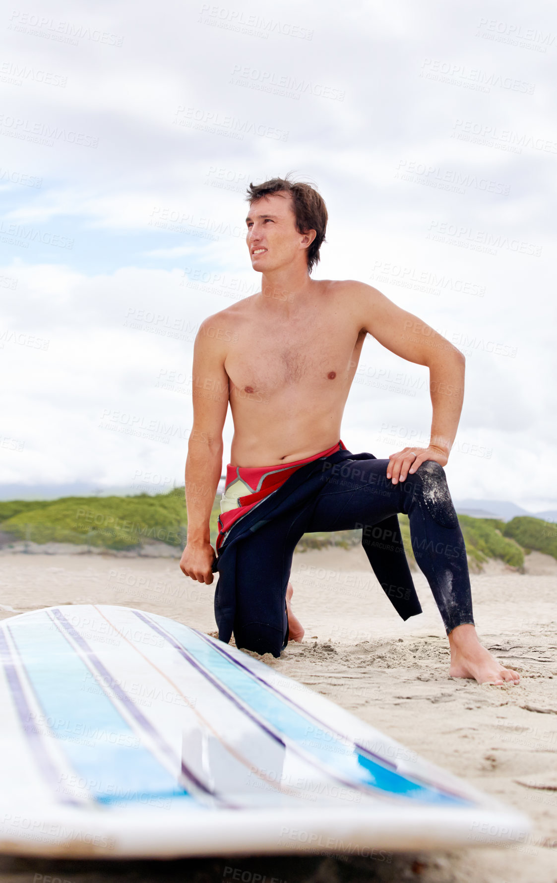 Buy stock photo A young surfer doing stretches on the beach next to his board