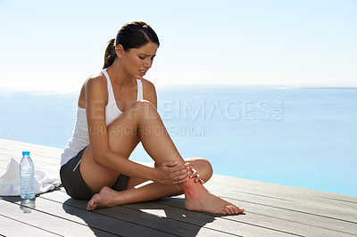 Buy stock photo An attractive young woman tending to her ankle injury on the pier