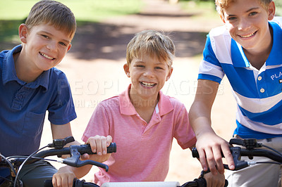 Buy stock photo Portrait of three young brothers riding their bicycles outside