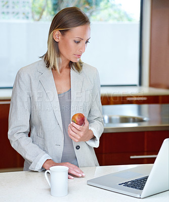 Buy stock photo A young woman standing by the kitchen counter with her laptop and a light breakfast