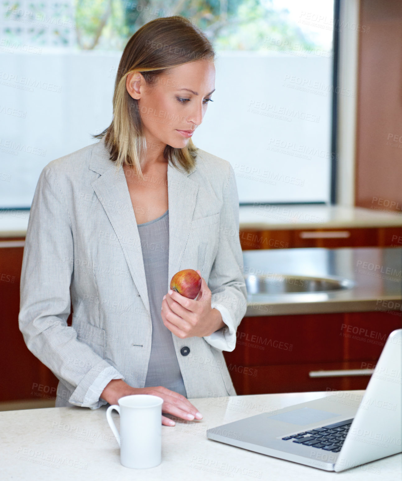Buy stock photo A young woman standing by the kitchen counter with her laptop and a light breakfast