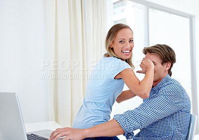 Buy stock photo A young woman covering her boyfriend's eyes as he works on a laptop