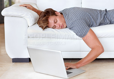 Buy stock photo A young man lying on his couch with his hand resting on his laptop's keyboard