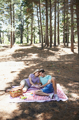 Buy stock photo Happy couple, relax and nature for picnic, love or support in affection, date or outdoor bonding. Young woman and man sitting on floor with basket of food for embrace, eating or romance in forest